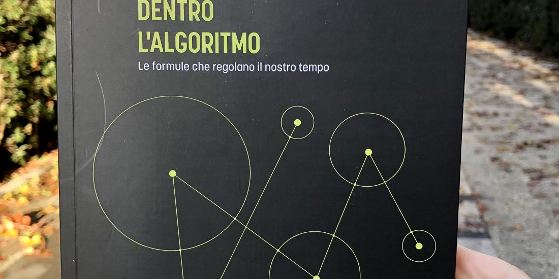 Il libro Dentro l'algoritmo tenuto in mano da me alle Mura Aureliane, a Roma. La copertina è nera, la scritta del titolo gialla e l'immagine raffigura un grafo (puntini uniti da linee a indicare le relazioni tra loro).