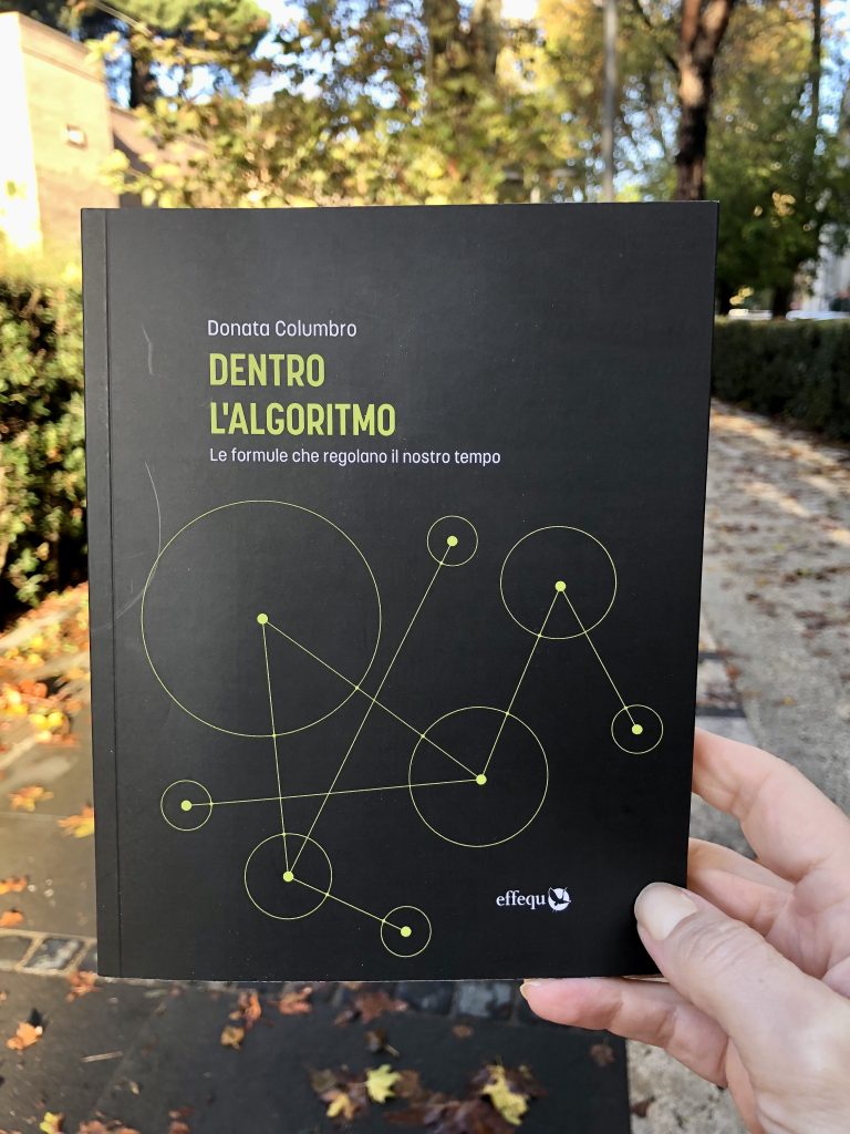 Il libro Dentro l'algoritmo tenuto in mano da me alle Mura Aureliane, a Roma. La copertina è nera, la scritta del titolo gialla e l'immagine raffigura un grafo (puntini uniti da linee a indicare le relazioni tra loro).